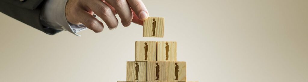 Businessman building a pyramid of wood blocks with people silhouettes